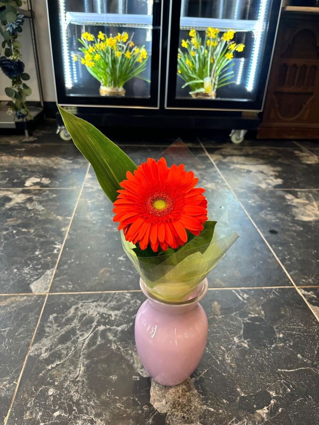 A single orange gerbera wrapped in a lilac vase
