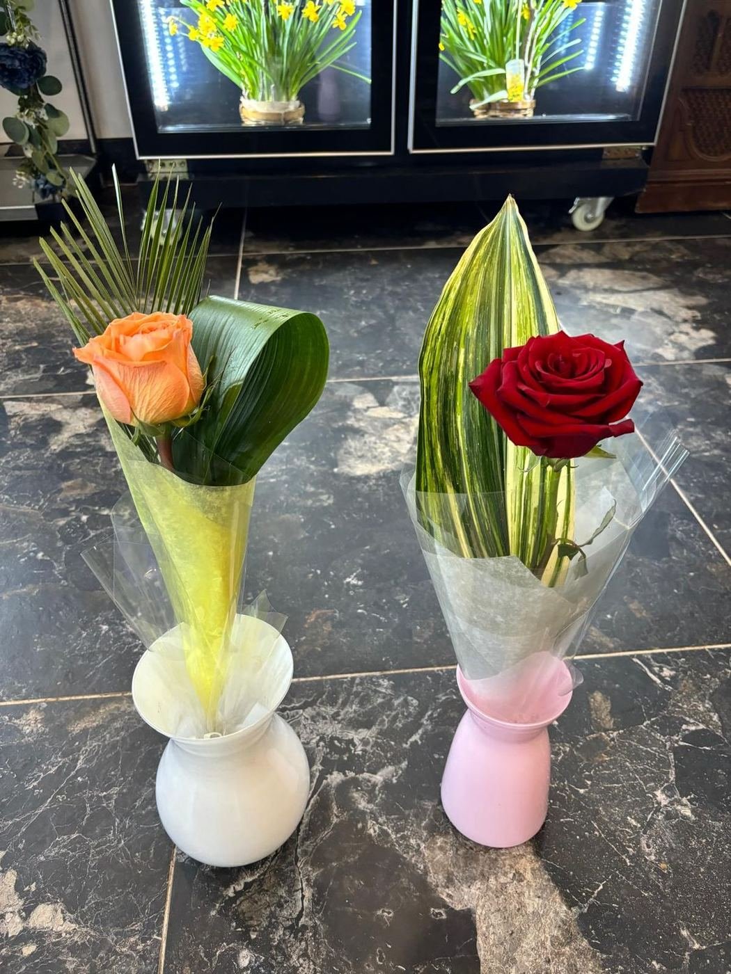 A peach rose and a red rose, each wrapped in a small vase