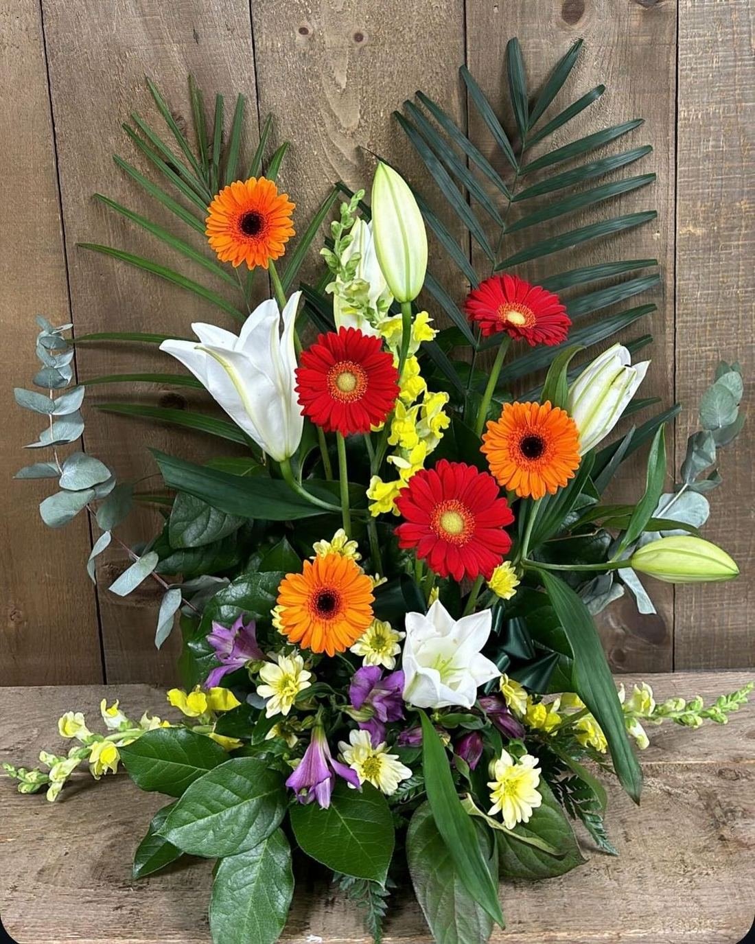 Orange and red gerberas with white lilies and palm leaves