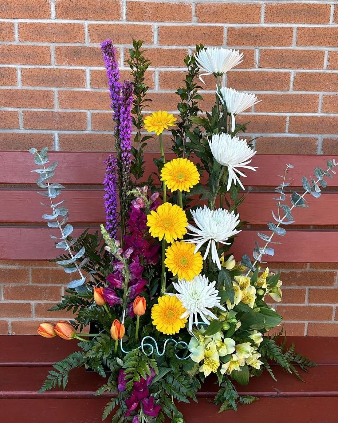 Garden arrangement of gerberas, liatris, tulips and chrysanthemums with a wire “love” accent